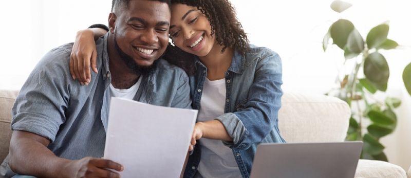 Couple noir positif lisant la documentation à la maison, vérifiant ensemble les détails de l