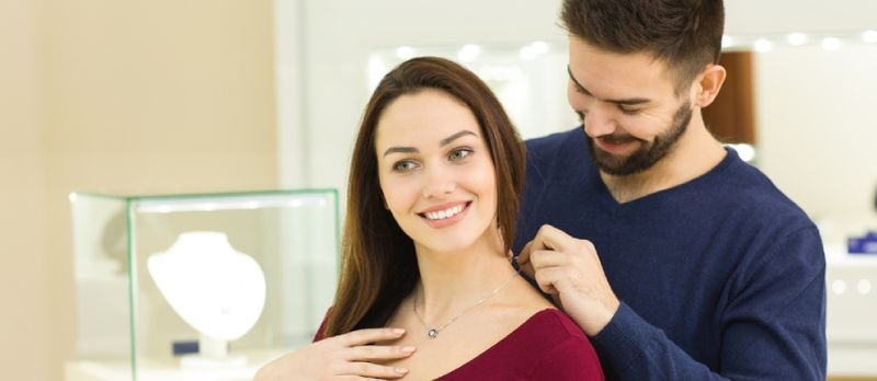 Bărbat care își ajută iubita să încerce un colier de aur