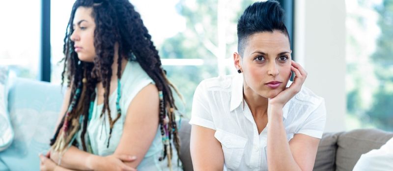Infeliz pareja lesbiana sentada en el sofá en la sala de estar