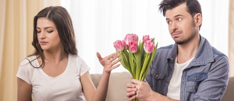 Il giovane sta offrendo un mazzo di fiori alla sua ragazza arrabbiata a casa.