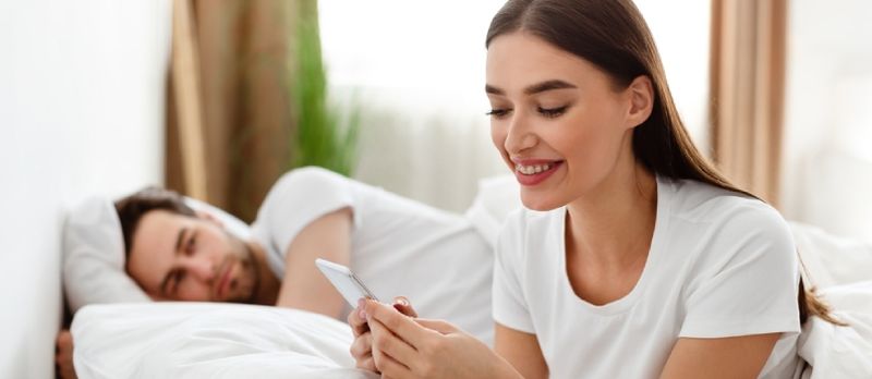 Une femme infidèle envoie des SMS au téléphone avec son amant pendant que son mari dort au lit à la maison