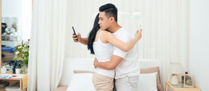 Fra siden av utro mann og kvinne jukser på telefonen mens de klemmer hverandre