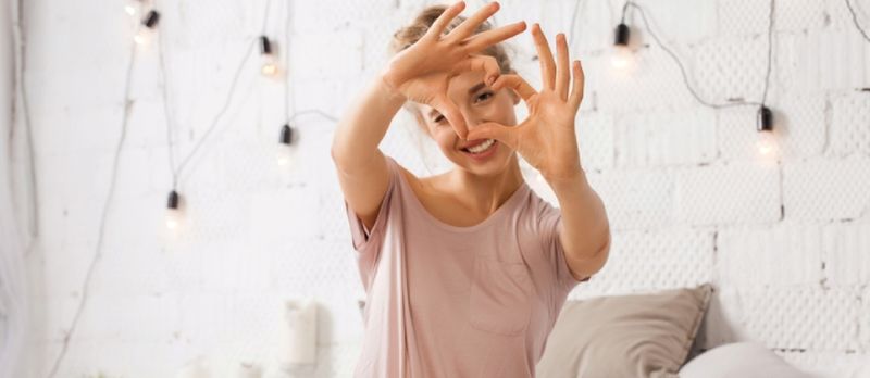 Belle Jeune Femme Assise Sur Le Lit Et Montre Geste Coeur Avec Les Doigts