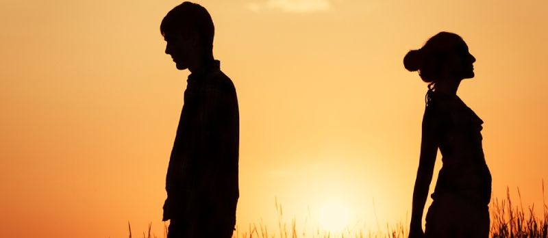 Couple debout contre le coucher du soleil dos à dos