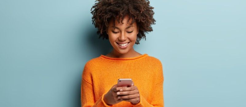 Meisie SMS op selfoon wat glimlag in die geel rok