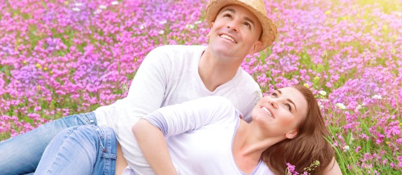 Casal feliz passando tempo ao ar livre, deitado e abraçando no lindo campo floral rosa, relacionamento romântico, conceito de amor