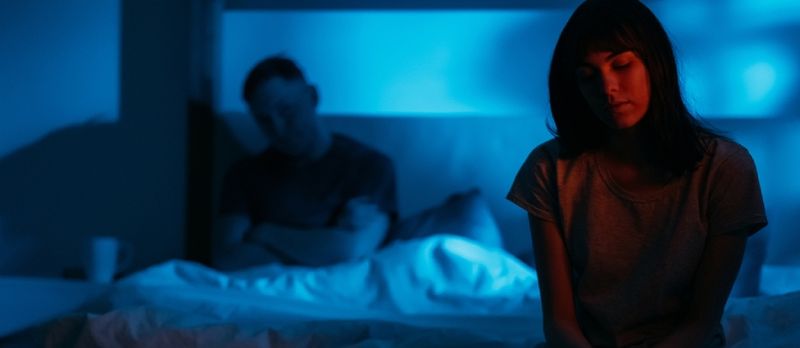Femme humiliée effrayée et peu sûre assise sur le lit à distance de l