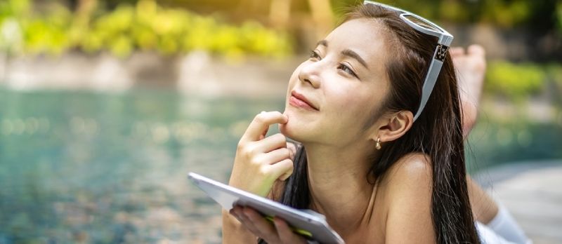 Linda mulher asiática com bom humor jogando um tablet na piscina e pensando no passado que o fez feliz