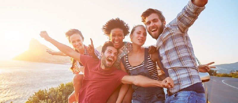 Grupa prijatelja stoji pored auta na obalnoj cesti u zalasku sunca