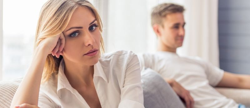 Belle jeune femme est assise triste sur un canapé à la maison, son petit ami est assis en arrière-plan