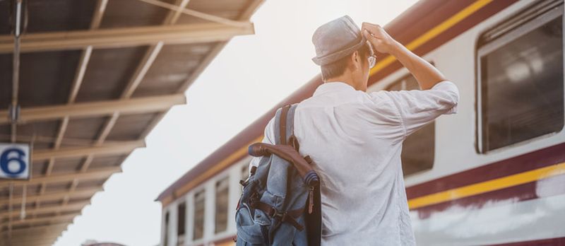 Sırt çantası ilə Qatar gözləyən Asiyalı Səyahətçi, Banqkok Qatar Stansiyasında Dəmiryol Platformasında Papaqlı Asiyalı Backpacker