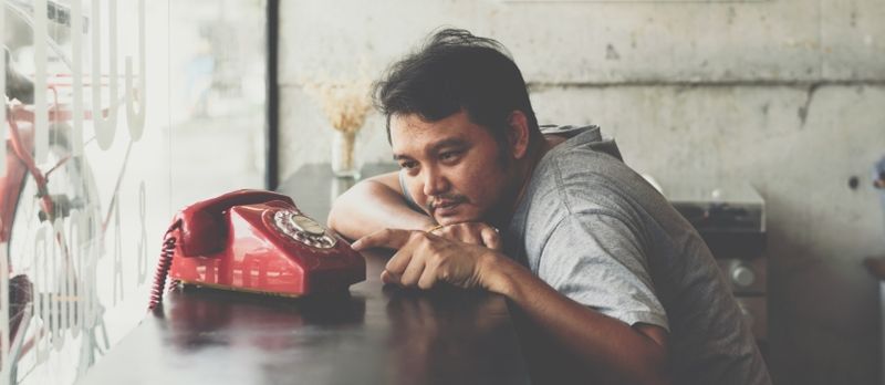 Bărbat asiatic 40 de ani în tricou gri Fericire cu timiditate și dragoste între așteptarea ceva sau așteptarea unui apel telefonic de la iubit într-o cafenea Cafenea cu un telefon roșu Stil vintage