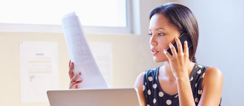 Gruaja që shikon letrat e punës ndërsa është në një telefonatë