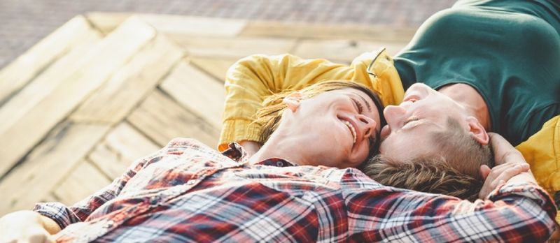 Glückliches schwules Paar, das auf einer Bank liegt und sich gegenseitig anschaut Junge lesbische Frauen, die einen zärtlichen romantischen Moment im Freien haben
