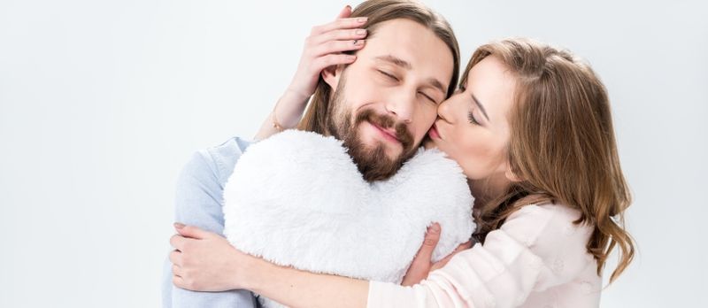 Jeune femme embrassant un homme qui tient un oreiller en forme de coeur