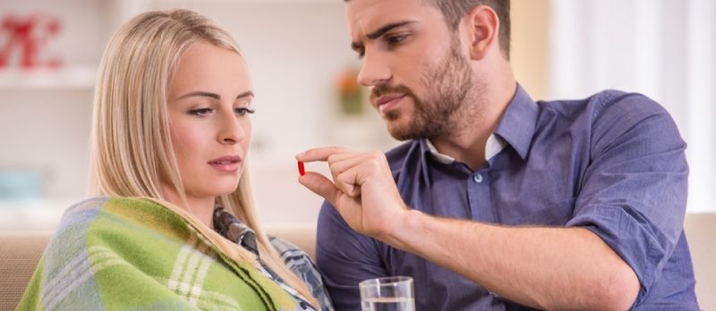 En mann hjelper en syk jente som sitter på sofaen hjemme