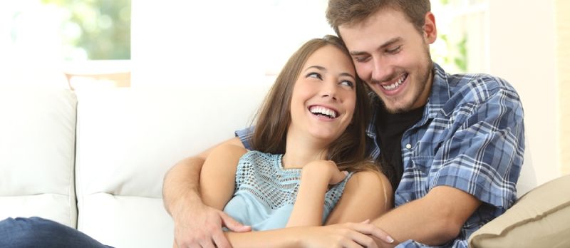 Felizes homens e mulheres amorosos sorrindo e sentados no sofá na sala de estar