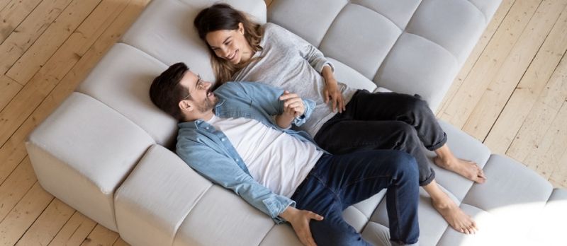 Pareja amorosa tomados de la mano, relajándose en un sofá acogedor en la vista superior de la sala de estar moderna
