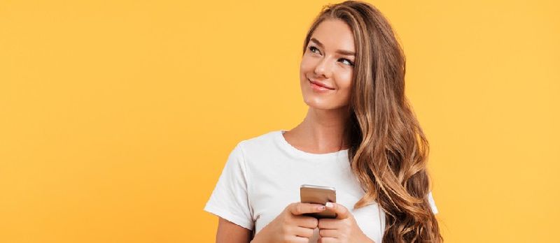 Foto av glad söt vacker ung kvinna som chattar med mobiltelefon isolerad över gul väggbakgrund