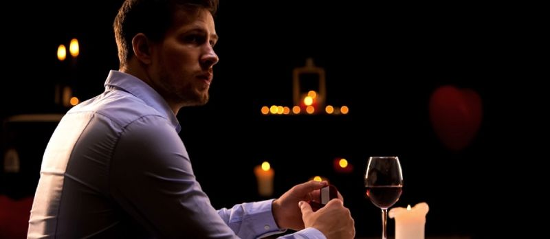 Mann mat Verlobungsring sëtzt eleng am Restaurant