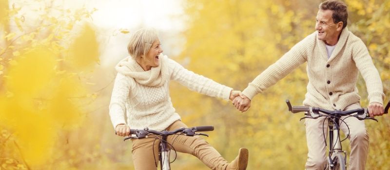 Seniori activi care merg cu bicicleta in natura de toamna. Se relaxează în aer liber