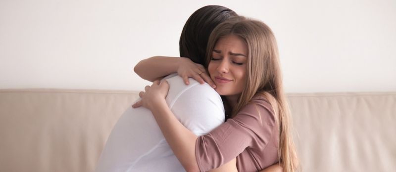 Portret emotivnog mladog para koji se čvrsto grli, dečko i djevojka se grle sjede na kauču