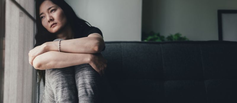Traurige verärgerte Dame, die in der Ecke des Fensters sitzt und nach draußen schaut