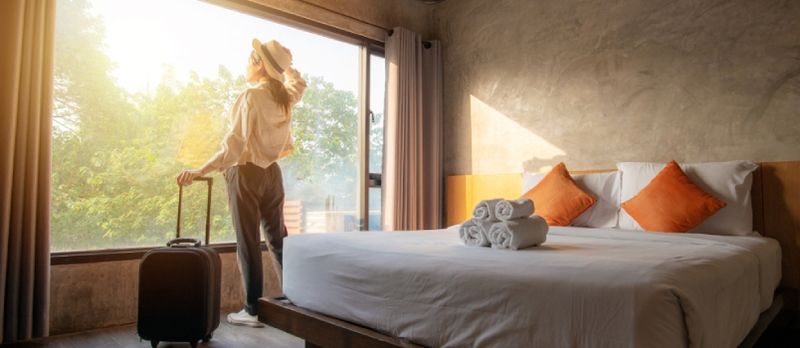 Porträt einer Touristenfrau, die fast am Fenster steht und mit ihrem Gepäck im Hotelzimmer auf eine schöne Aussicht blickt