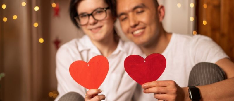 Chico y chica felices sentados en el suelo y sosteniendo corazones rojos. Concepto de amor