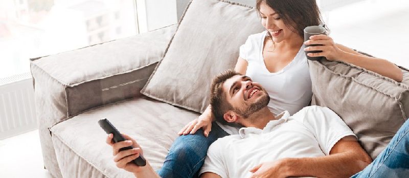Alegre hermosa pareja joven tomando café y viendo la televisión en casa
