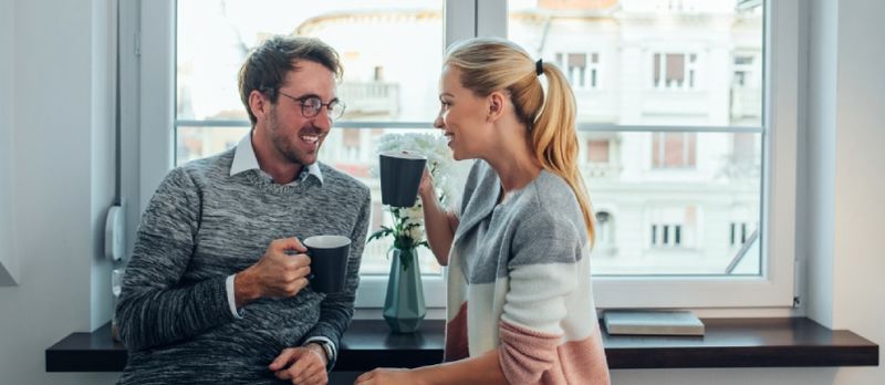 Fröhliches Paar, das zusammen hinter dem Fenster Kaffee trinkt und mit einem Liebesmoment zusammen plaudert