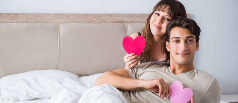 Couple heureux dans le lit tenant du papier coeur rouge