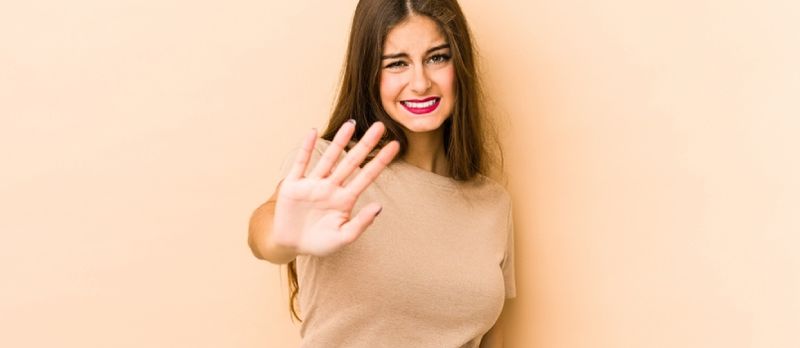 Mlada kavkaska žena izolirana na bež pozadini odbija nekoga ko pokazuje gest gađenja