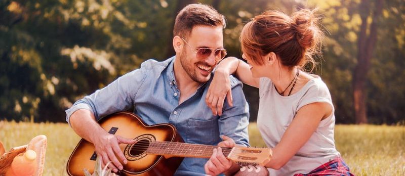 Mężczyzna gra na gitarze, podczas gdy kobieta patrzy na niego i się uśmiecha