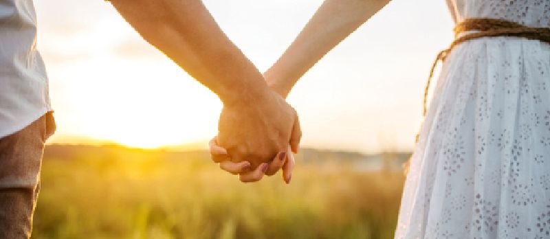 Hombres y mujeres tomados de la mano juntos se paran juntos en el campo con una hermosa puesta de sol