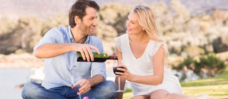 Para na randce nalewająca czerwone wino leżąc na kocu