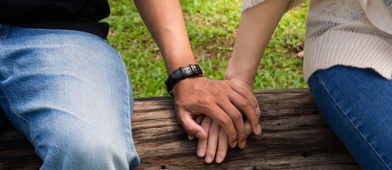 Junges Paar, das Hand hält, während es arbeitet oder Zeit im Freien Plublic Park im warmen Sommertageslicht verbringt